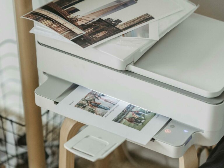 A cozy home office corner with a printer, coffee cup, and printed photos on a wooden table.